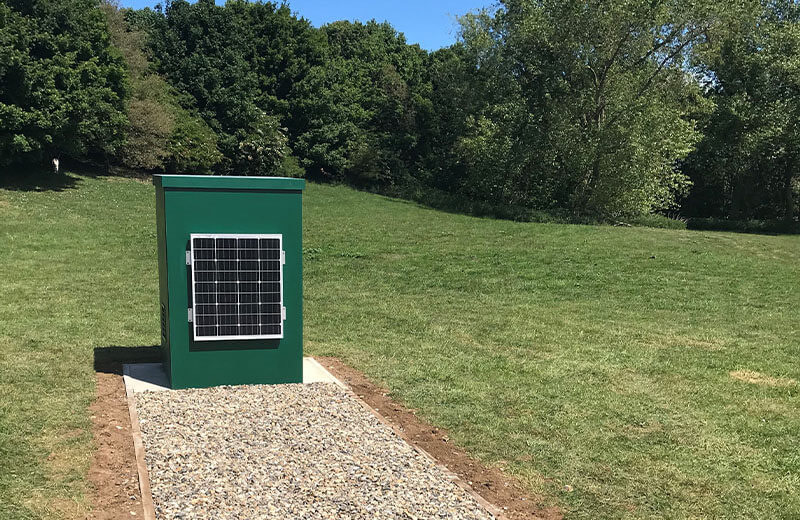 A green GRP renewable energy housing with a solar panel, on a gravel base
